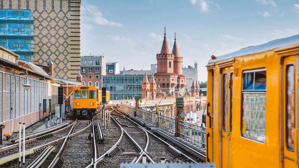 A train station with multiple tracks, a yellow train, and a historic building with towers in the background.