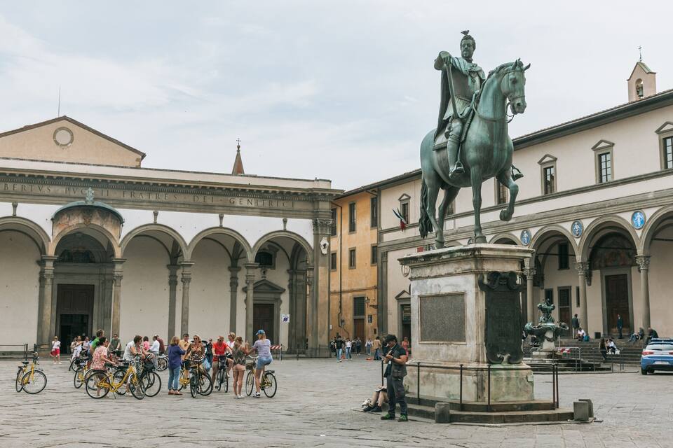 A statue of a man on horseback in a public square with people and bicycles around.