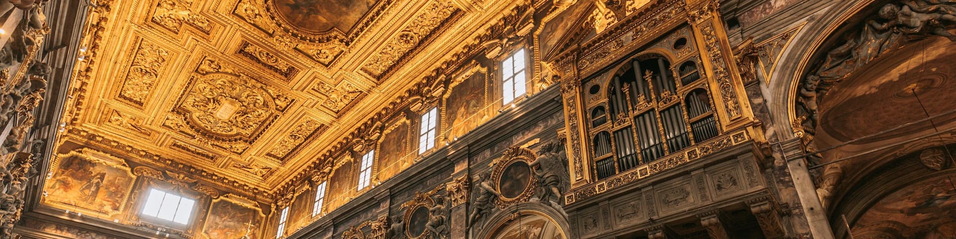 Interior ornamentado de una iglesia con frescos detallados, detalles dorados y un órgano grande.