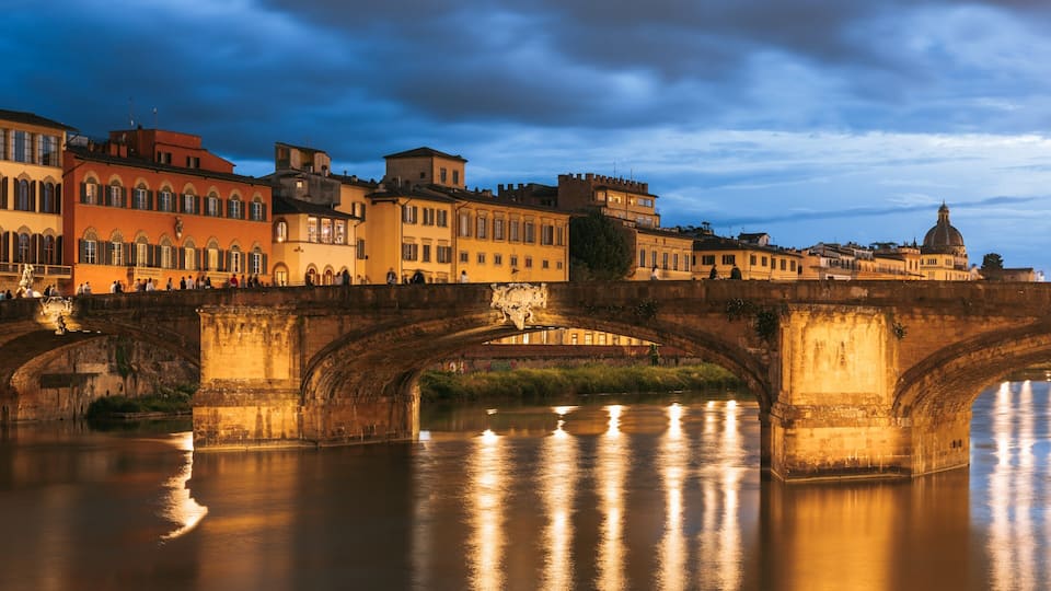 A stone bridge over a calm river, with historic buildings on either side.