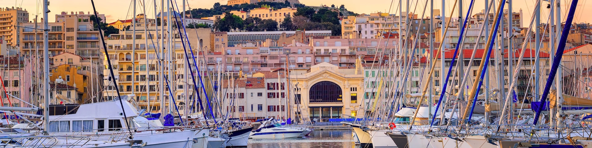 A marina with numerous sailboats docked, a prominent church with a bell tower, and a hilltop building in the background.