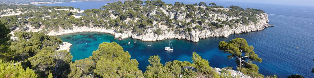 A coastal landscape with a rocky island surrounded by clear blue waters, dense green trees, and a small boat anchored near the shore.