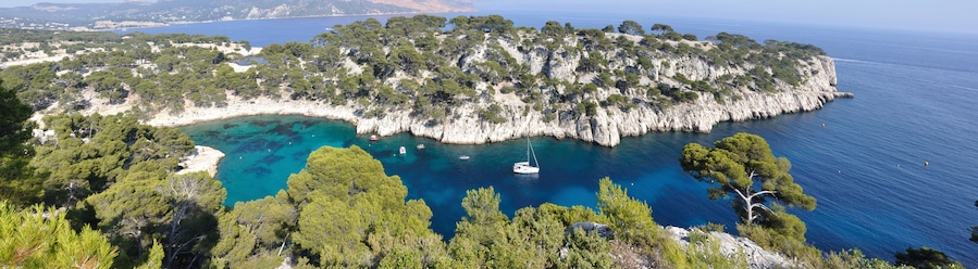 Paisagem costeira com uma ilha rochosa cercada por águas azuis cristalinas, árvores verdes densas e um pequeno barco ancorado perto da costa.