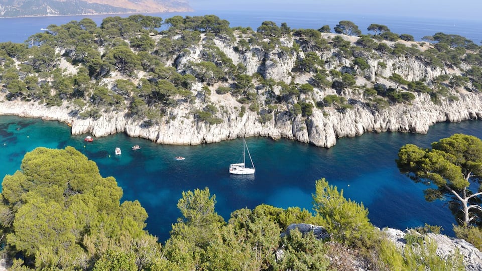 A coastal landscape with a rocky island surrounded by clear blue waters, dense green trees, and a small boat anchored near the shore.