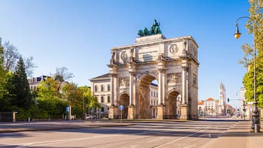A grand archway with statues, surrounded by trees and buildings.