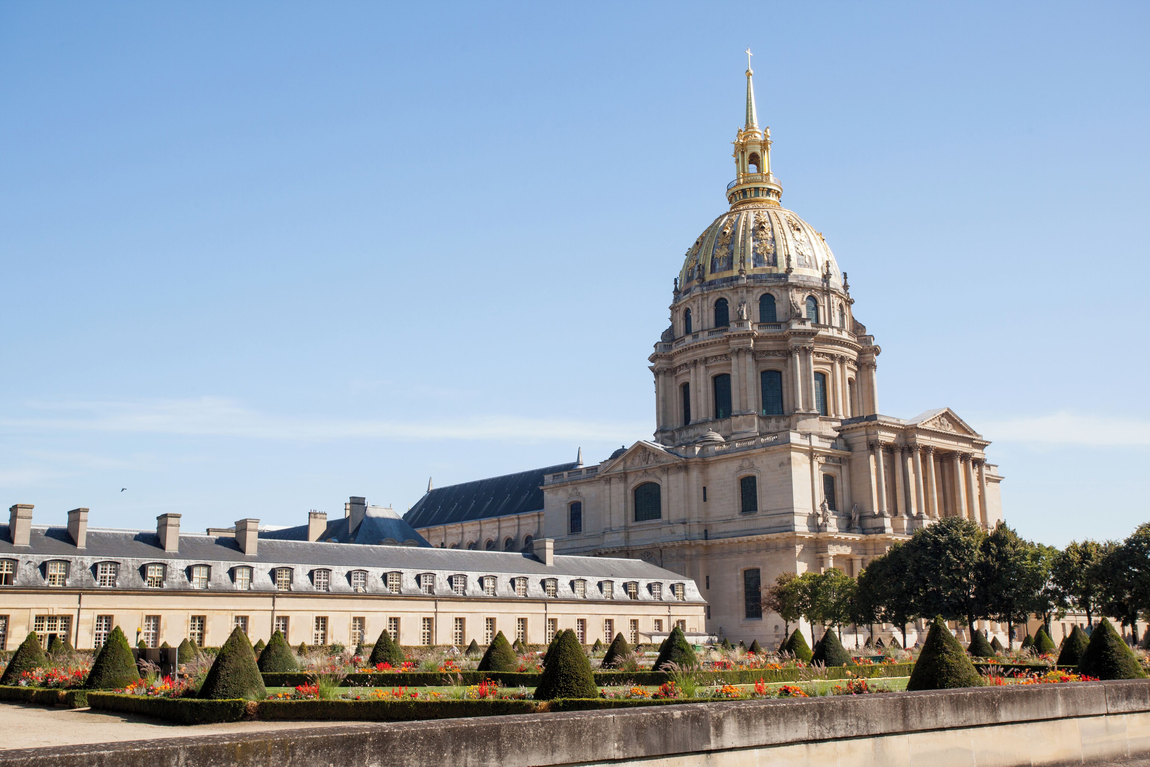 A historic building with a prominent dome and a symmetrical garden with topiary trees.