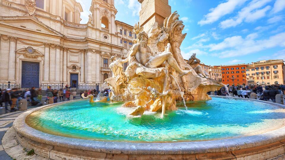 A large fountain with sculptures in a public square, surrounded by historic buildings.