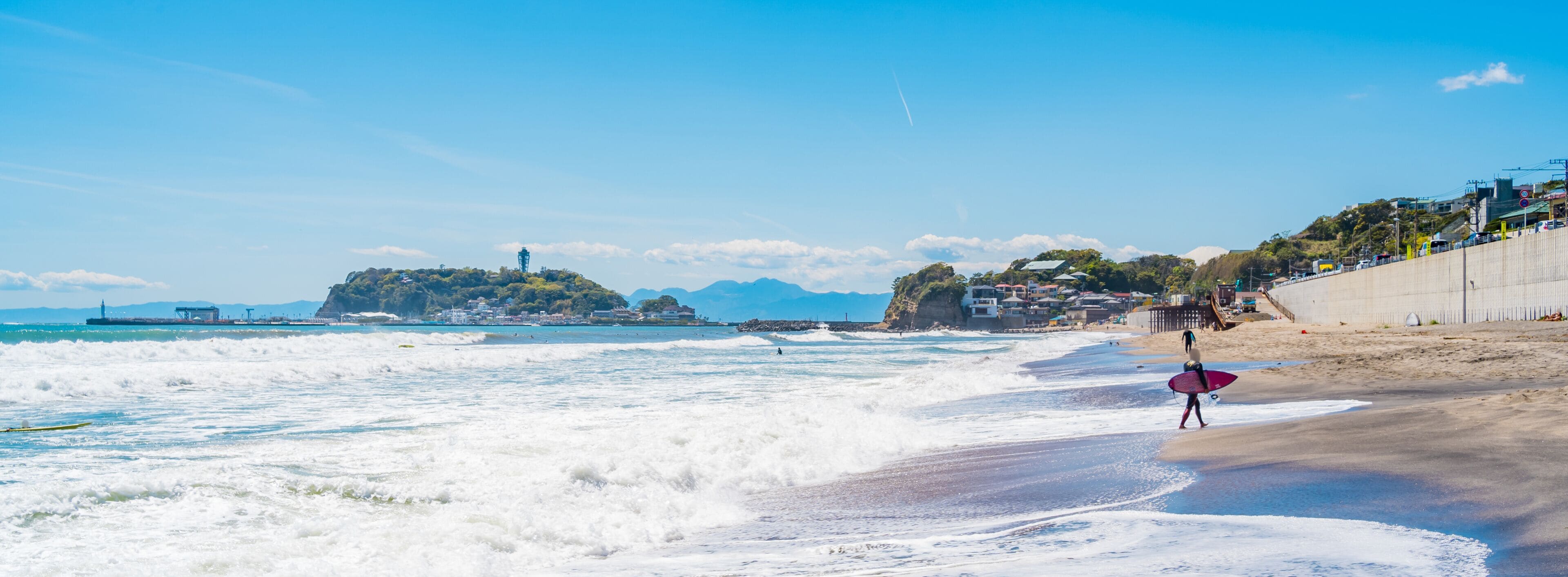 A beach with waves, a lighthouse, and a coastal town.