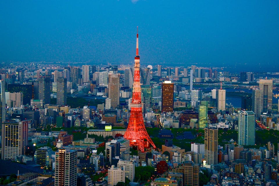 A cityscape with a prominent red-lit tower, dense urban buildings, and a river in the background.