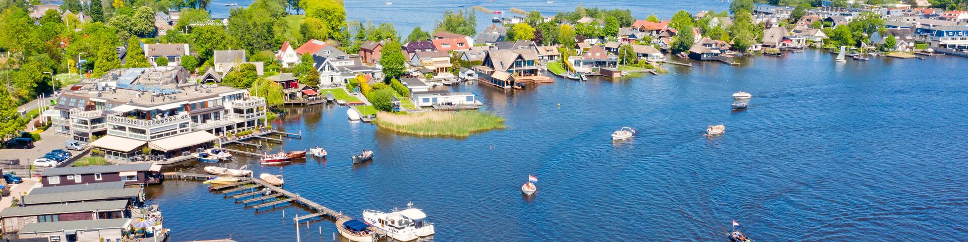 A river town with boats docked along the waterfront, surrounded by greenery and residential buildings.