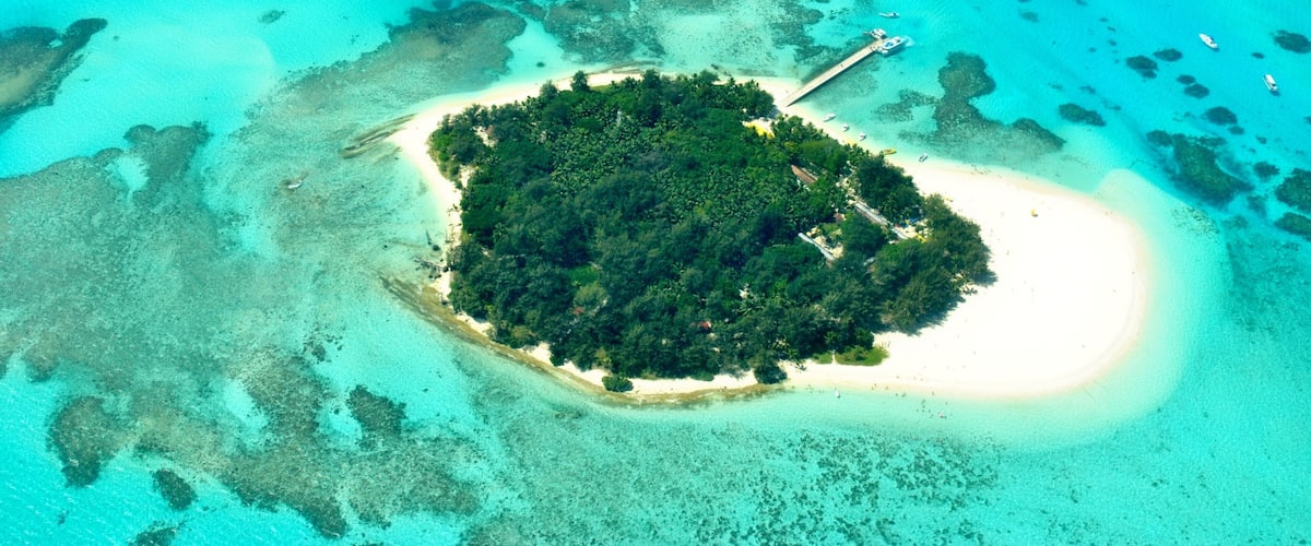 An aerial view of a small island with a white sandy beach surrounded by turquoise waters and coral reefs.
