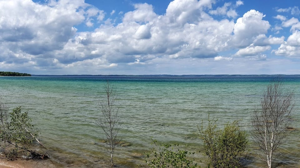 A coastal landscape with clear turquoise waters, rocky shoreline, and sparse vegetation.