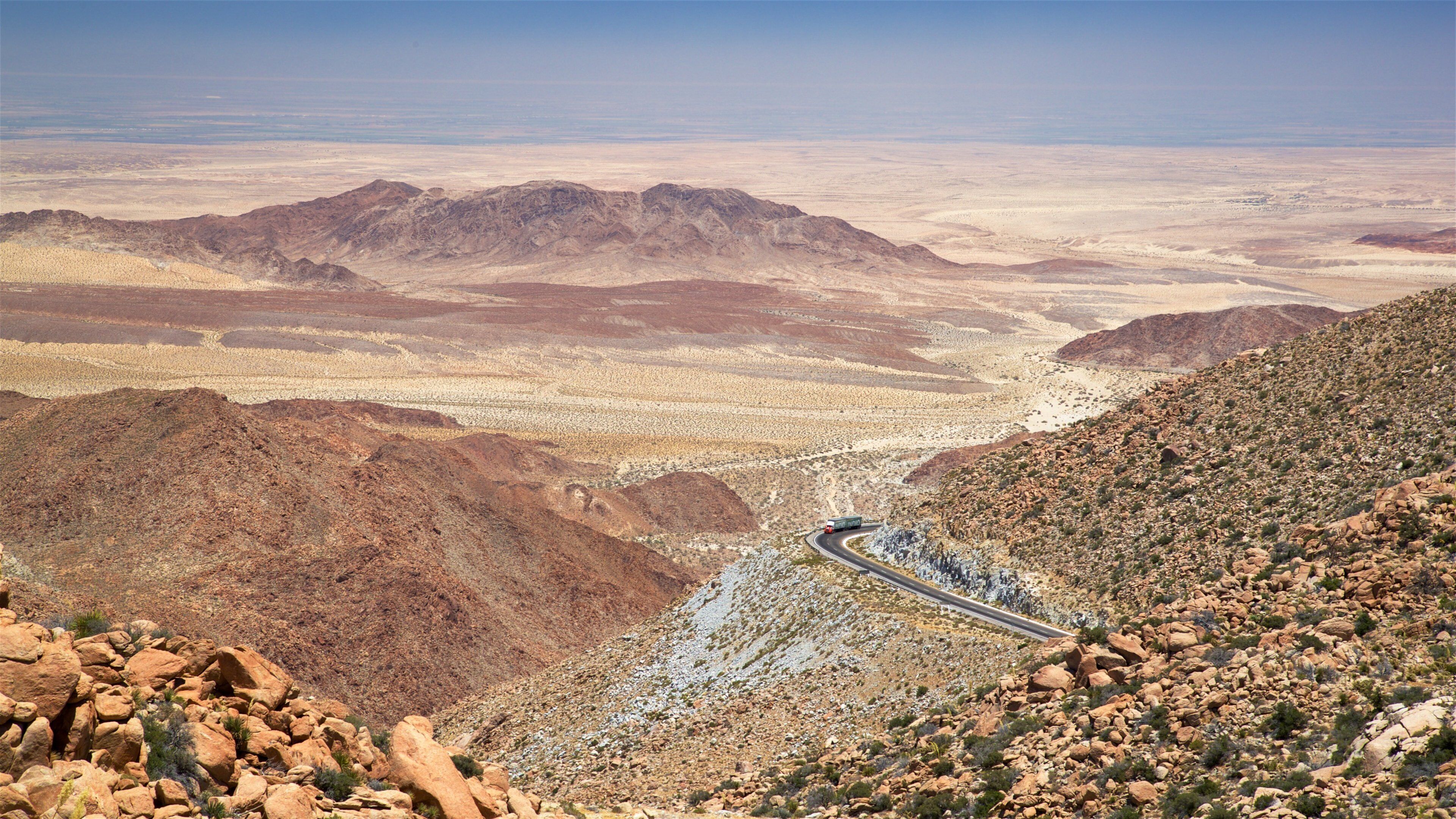 A winding road through a desert landscape with rocky terrain and distant mountains.