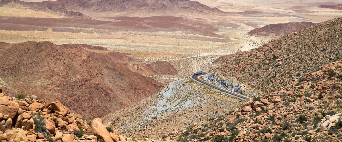 A winding road through a desert landscape with rocky terrain and distant mountains.