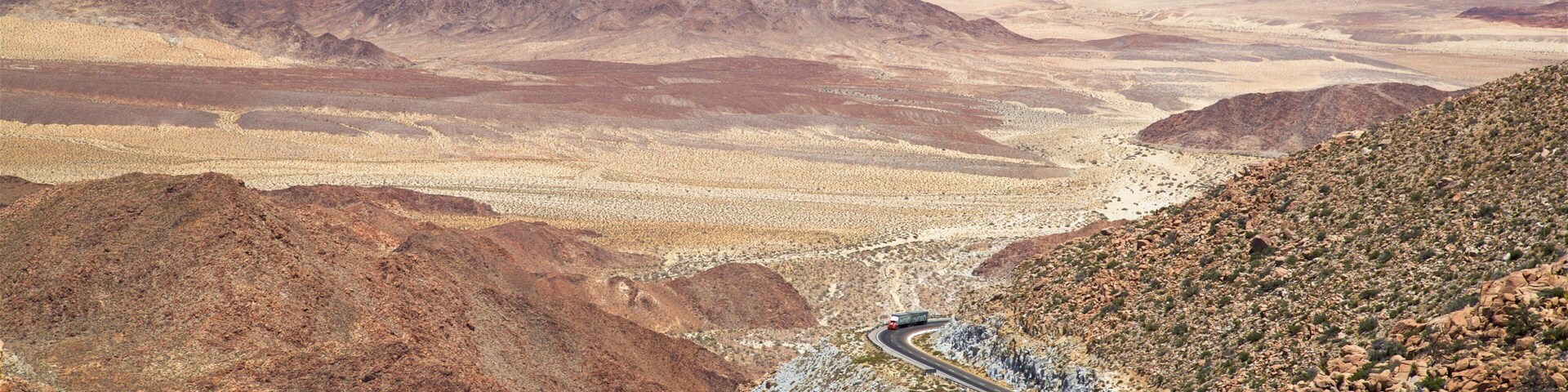 A winding road through a desert landscape with rocky terrain and distant mountains.