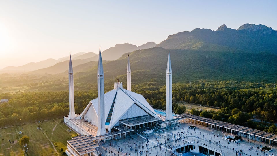 A mosque with four minarets and a large courtyard surrounded by mountains.