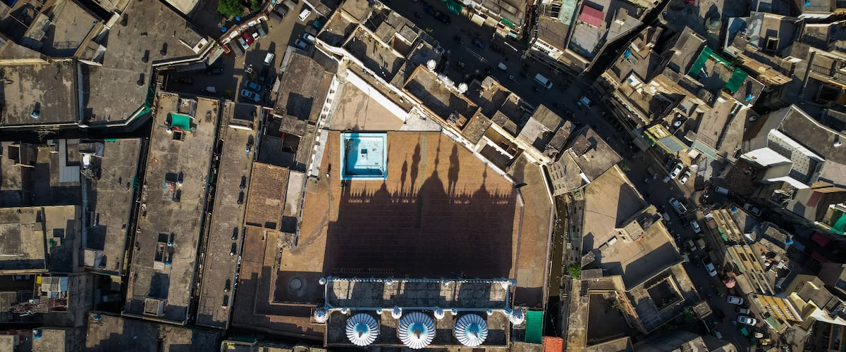 An aerial view of a densely packed urban area with narrow streets, a large open square, and a prominent building with a blue roof.