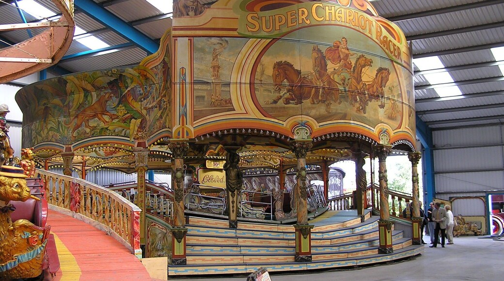 Edwards’ Super Chariot Racer at Dingles Fairground Heritage Centre, Lifton, Devon Robert Edwards ordered the ride new in 1934 at a cost of £1,750. It was built in Burton on Trent by Messrs. Orton, Sons and Spooner. The ride is 42 feet in diameter, plus the porch and steps, and was decorated in art deco ‘jazz’ style, popular in the 1930s. After the war the ride was rebuilt with the massive Chariot Racer scene on the front boards. This was constructed at Ortons and painted by their artists, Sid and Albert Howell. The Chariot Racer was travelled by the Edwards family until 1991 when it was placed in store in Swindon until acquired by the Fairground Heritage Trust. It arrived at the site in 2006 and with the help of Frank Edwards, it was assembled within a fortnight of arriving at its new home, and opened to the public later that year. fairground-heritage.org.uk/