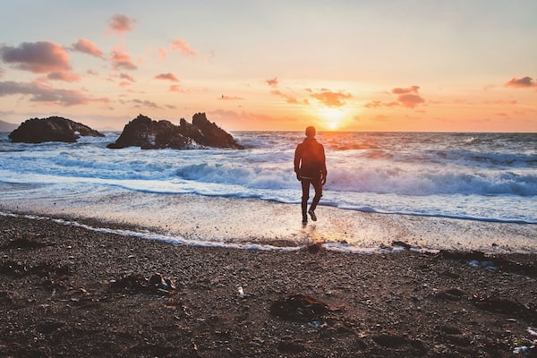 Eine Person geht bei Sonnenuntergang über einen steinigen Strand.