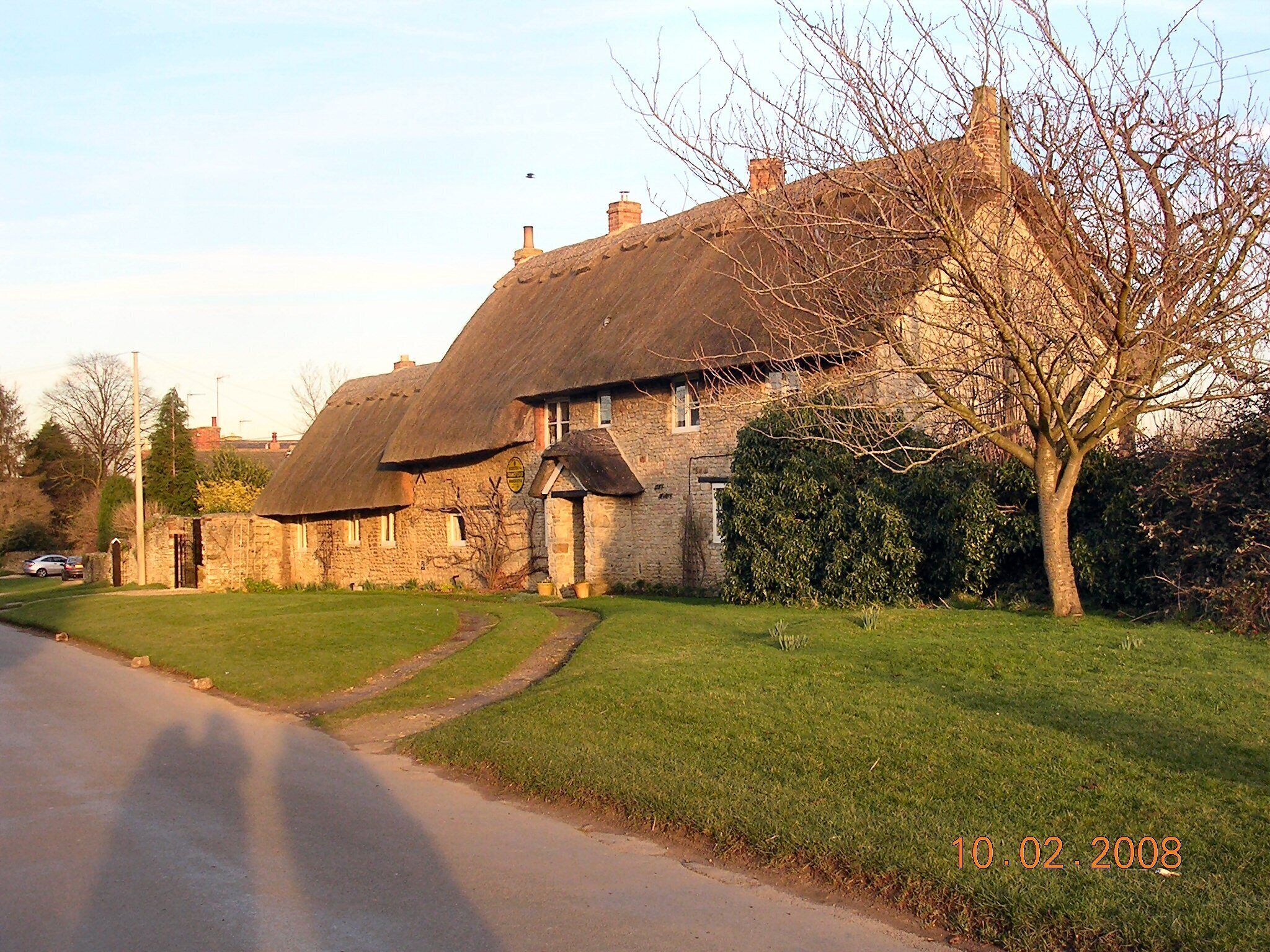A stone house with a thatched roof, surrounded by a grassy lawn and a tree.