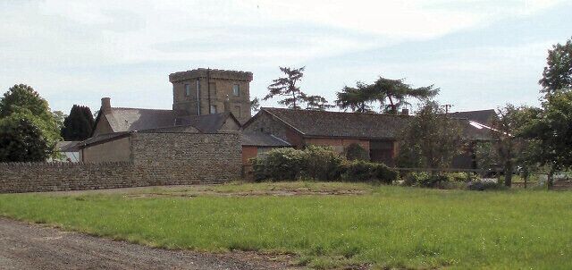 A stone building with a tower, surrounded by green fields and trees.