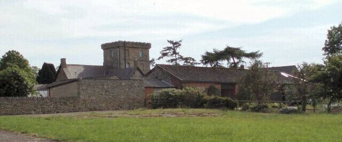A stone building with a tower, surrounded by green fields and trees.