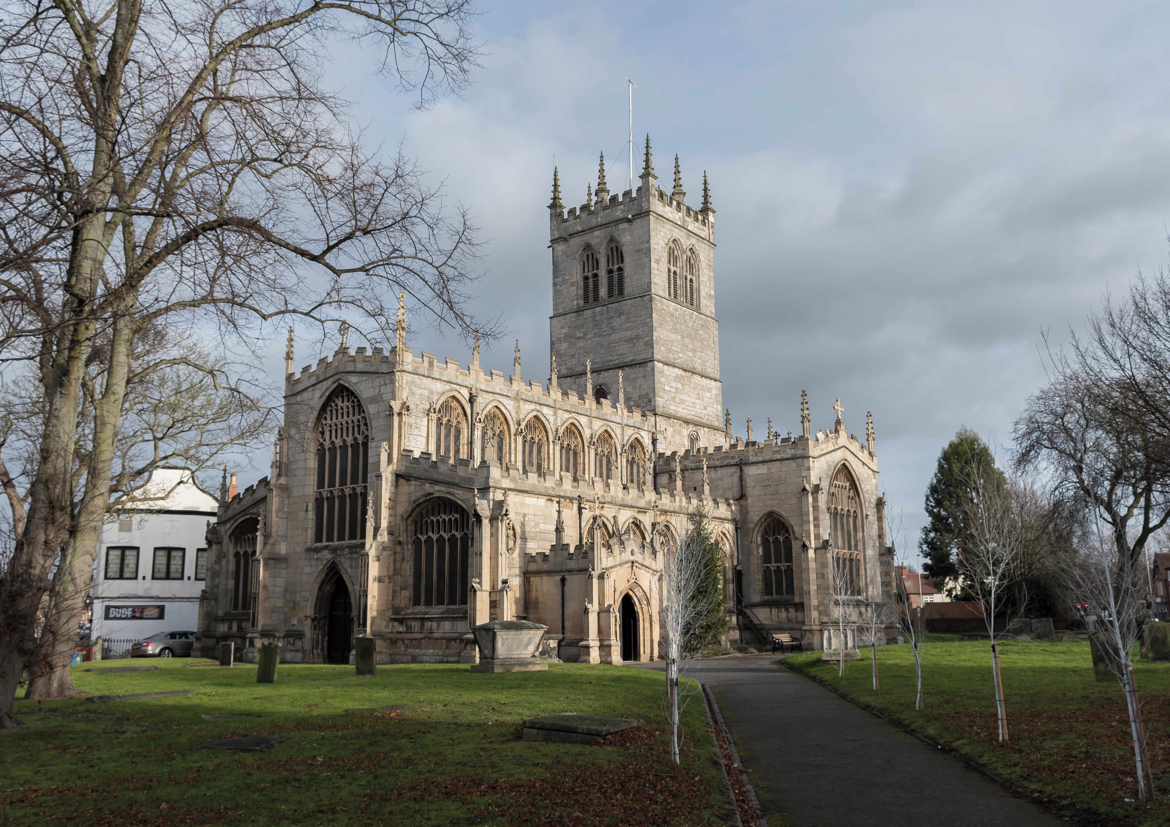 The first record of the church is in 1258, and the oldest floor slab Memorial dates from 1496. This large church is now mostly the work of a 17th-century restoration, after the tower collapsed in 1651 destroying much of the chancel and south transept. It was rebuilt in 1658. The church is in a cruciform plan with north and south transepts, a central four stage crossing tower, nave with north and south aisles and clerestory windows, chancel, and south porch. There is also a Lady Chapel, Vestry and Sacristy. The oldest part of the church is the north transept which has two arches and an octagonal pier with fine leaf decoration on the capital. This was revealed during a restoration in 1873. The four bay chancel was refurbished around the same time, and it was extended to its original size. The north aisle was rebuilt using original material as well as the clerestory, battlements, and other parts church in 1854. The south porch was also added. There was further restoration in 1905. The church has numerous stained glass windows from the nineteenth century by several well-known artists. The west window of the south transept contains mediaeval glass, and is unusual in having two coins set into the glass. The organ was originally on a gallery at the west end, and in 1841 a new organ was placed on the south side of chancel. It was subsequently enlarged and has been overhauled several times since. In 1980 it was completely rebuilt with a new movable console. The tower has a ring of 10 bells. In 2009 a toilet and kitchen were installed in the west end of church. In 2010 the nave and south aisle roofs were repaired with the aid of a grant from English Heritage.