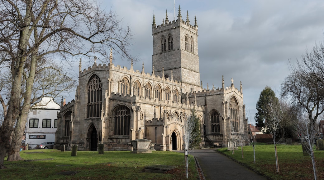The first record of the church is in 1258, and the oldest floor slab Memorial dates from 1496. This large church is now mostly the work of a 17th-century restoration, after the tower collapsed in 1651 destroying much of the chancel and south transept. It was rebuilt in 1658. The church is in a cruciform plan with north and south transepts, a central four stage crossing tower, nave with north and south aisles and clerestory windows, chancel, and south porch. There is also a Lady Chapel, Vestry and Sacristy. The oldest part of the church is the north transept which has two arches and an octagonal pier with fine leaf decoration on the capital. This was revealed during a restoration in 1873. The four bay chancel was refurbished around the same time, and it was extended to its original size. The north aisle was rebuilt using original material as well as the clerestory, battlements, and other parts church in 1854. The south porch was also added. There was further restoration in 1905. The church has numerous stained glass windows from the nineteenth century by several well-known artists. The west window of the south transept contains mediaeval glass, and is unusual in having two coins set into the glass. The organ was originally on a gallery at the west end, and in 1841 a new organ was placed on the south side of chancel. It was subsequently enlarged and has been overhauled several times since. In 1980 it was completely rebuilt with a new movable console. The tower has a ring of 10 bells. In 2009 a toilet and kitchen were installed in the west end of church. In 2010 the nave and south aisle roofs were repaired with the aid of a grant from English Heritage.