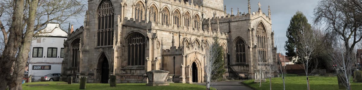 The first record of the church is in 1258, and the oldest floor slab Memorial dates from 1496. This large church is now mostly the work of a 17th-century restoration, after the tower collapsed in 1651 destroying much of the chancel and south transept. It was rebuilt in 1658. The church is in a cruciform plan with north and south transepts, a central four stage crossing tower, nave with north and south aisles and clerestory windows, chancel, and south porch. There is also a Lady Chapel, Vestry and Sacristy. The oldest part of the church is the north transept which has two arches and an octagonal pier with fine leaf decoration on the capital. This was revealed during a restoration in 1873. The four bay chancel was refurbished around the same time, and it was extended to its original size. The north aisle was rebuilt using original material as well as the clerestory, battlements, and other parts church in 1854. The south porch was also added. There was further restoration in 1905. The church has numerous stained glass windows from the nineteenth century by several well-known artists. The west window of the south transept contains mediaeval glass, and is unusual in having two coins set into the glass. The organ was originally on a gallery at the west end, and in 1841 a new organ was placed on the south side of chancel. It was subsequently enlarged and has been overhauled several times since. In 1980 it was completely rebuilt with a new movable console. The tower has a ring of 10 bells. In 2009 a toilet and kitchen were installed in the west end of church. In 2010 the nave and south aisle roofs were repaired with the aid of a grant from English Heritage.