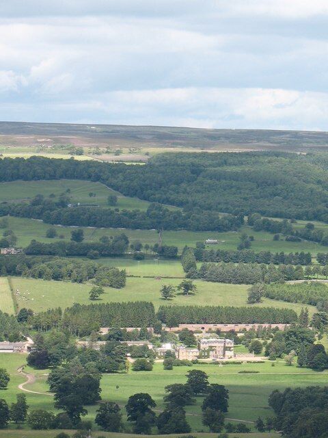 Un paisaje rural con colinas onduladas, un pequeño pueblo y una gran propiedad con un edificio destacado.