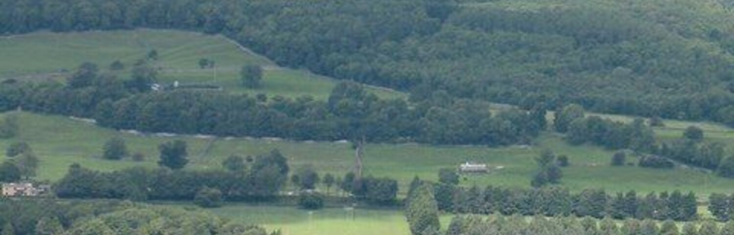 Un paisaje rural con colinas onduladas, un pequeño pueblo y una gran propiedad con un edificio destacado.
