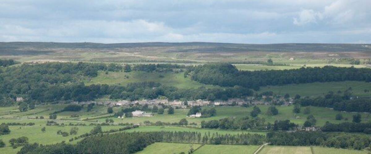 A rural landscape with rolling hills, scattered houses, and dense forests.