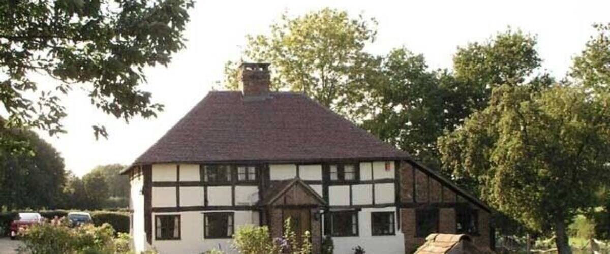A traditional half-timbered house with a green lawn and a wooden gazebo.
