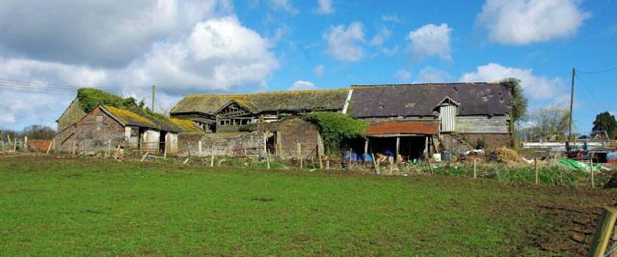 A rural farm with old stone buildings, a fenced field, and a clear blue sky.