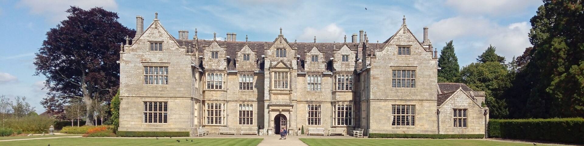 A large stone building with a symmetrical facade, a central entrance, and a well-maintained lawn with a gravel path leading to it.