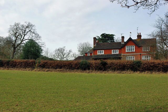 Una casa roja con techo negro, rodeada por un campo verde y un seto.