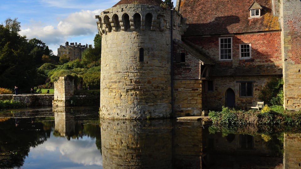 A historic castle with a moat, stone tower, and red-tiled roof.
