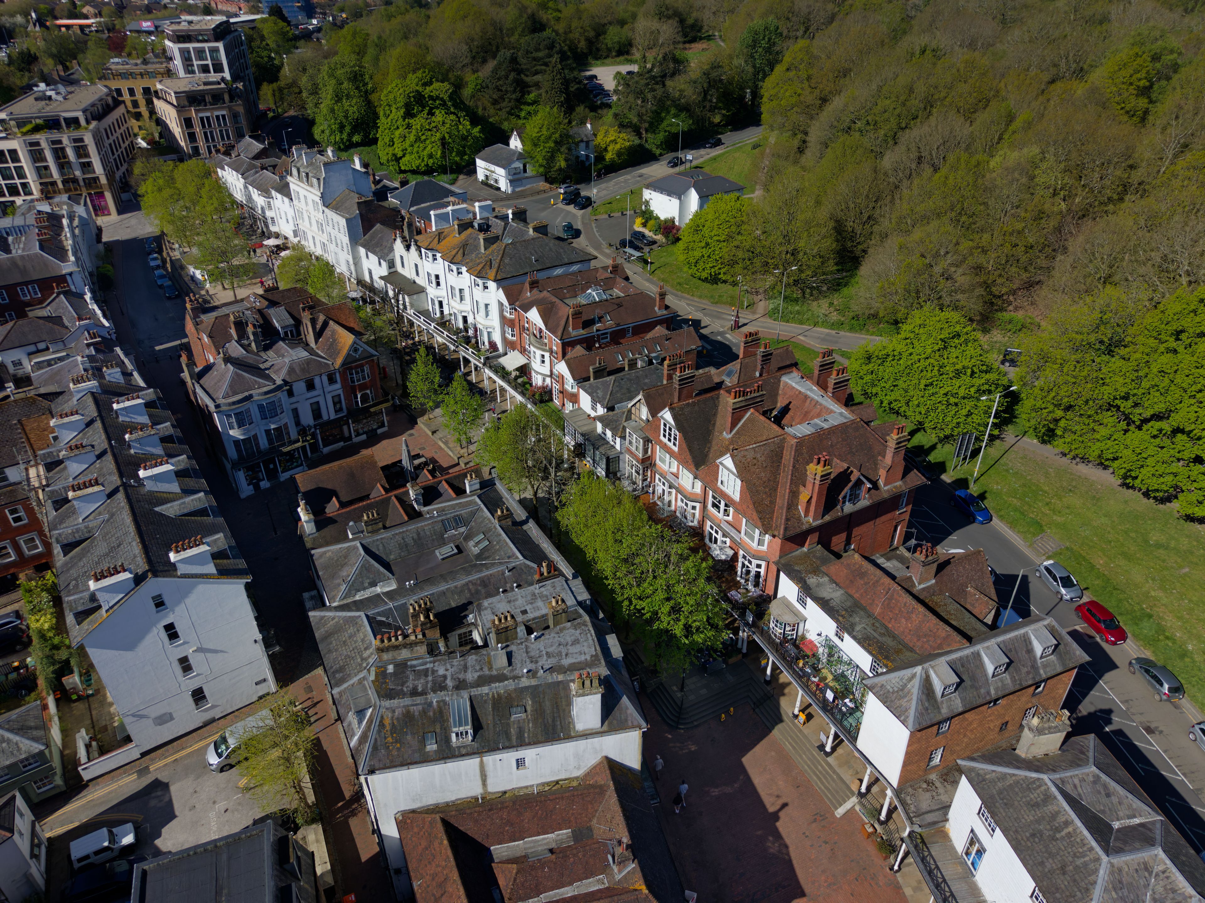 An aerial view of a town with a mix of residential and commercial buildings, a main road, and surrounding greenery.