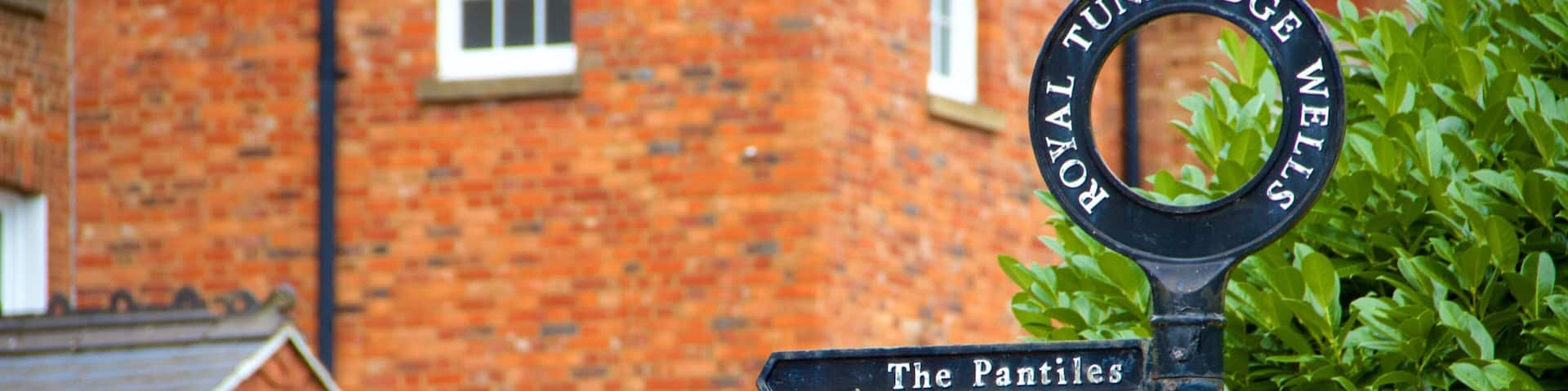 A signpost with 'ROYAL TUNBRIDGE WELLS' and 'The Pantiles' written on it, in front of a brick building.