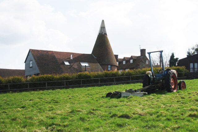 A conical building, a tractor, and a grassy field with a fence.