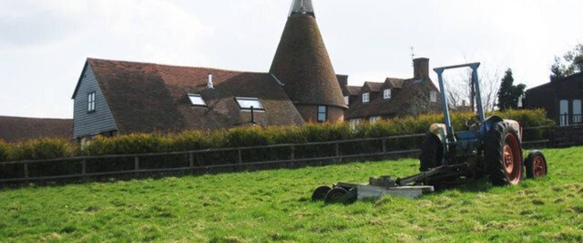 A conical building, a tractor, and a grassy field with a fence.