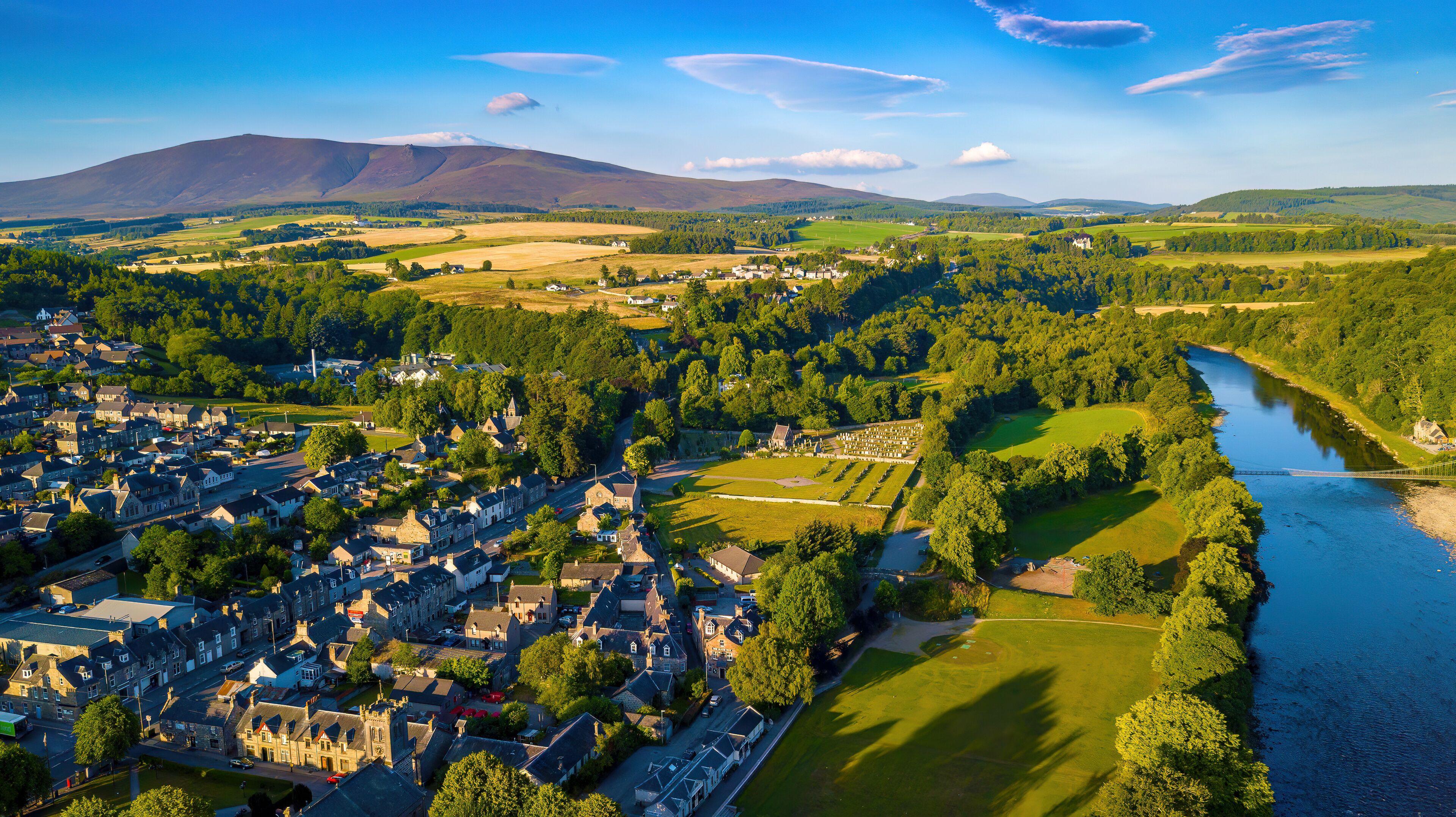 Aerial view of serene town by the river with greenery and hills, Aberlour, Scotland.