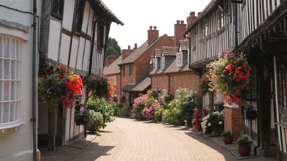 A narrow cobblestone street lined with traditional half-timbered houses, some with hanging flower baskets.
