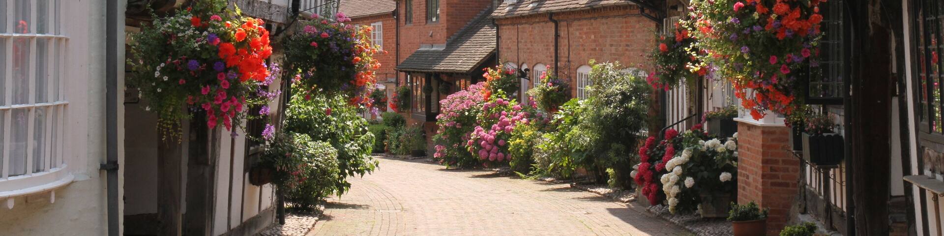 Half Timbered, Black & White Houses in Shakespeare's Country Malt Mill Lane Alcester Warwickshire, UK. Hanging baskets & floral blooms in High Summer.