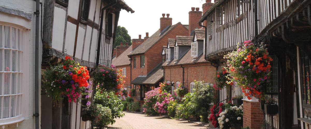 A narrow cobblestone street lined with traditional half-timbered houses, some with hanging flower baskets.