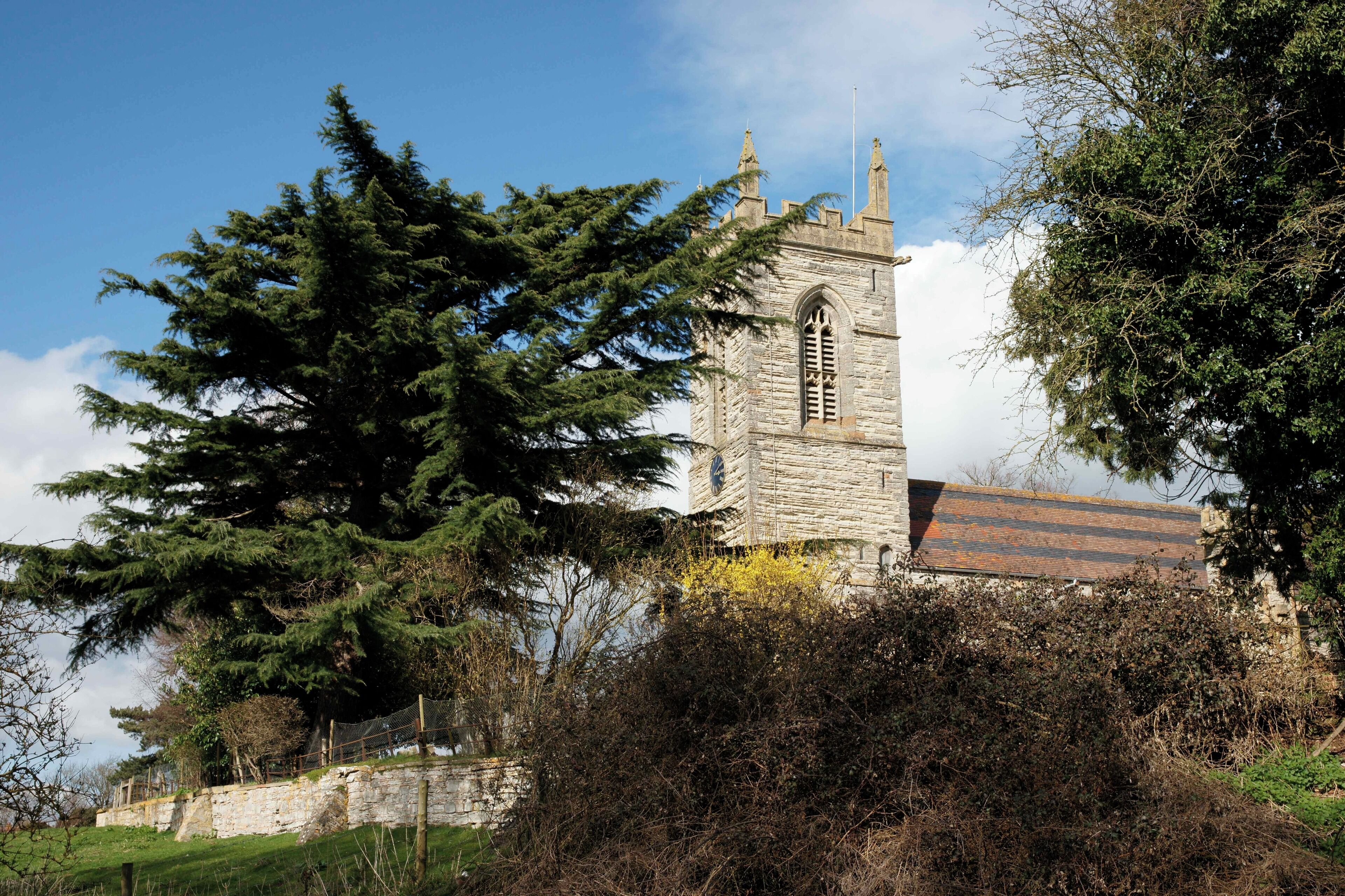 A stone church with a bell tower, surrounded by trees and a stone wall.