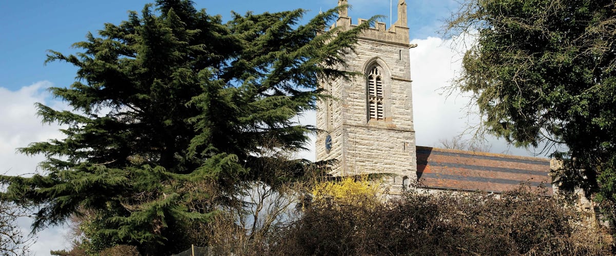 A stone church with a bell tower, surrounded by trees and a stone wall.
