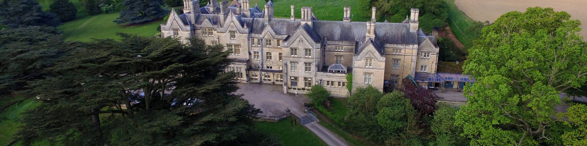 A large, historic building surrounded by lush greenery and rolling hills.