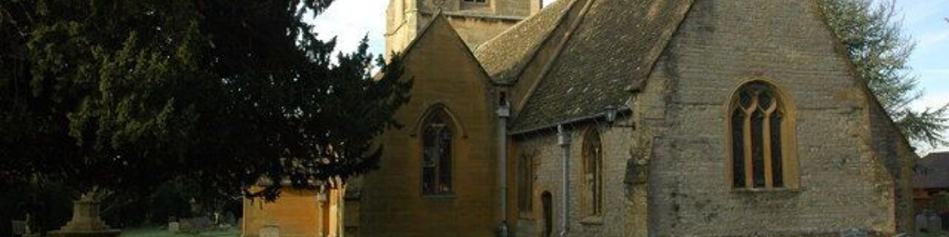 A church with a tall tower and a large tree in the foreground.