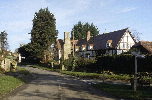 A quiet village street with traditional half-timbered houses, a large tree, and a clear blue sky.